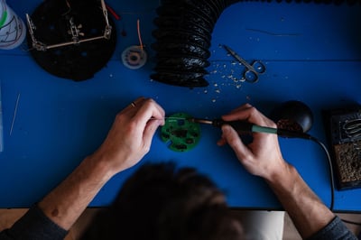 A pair of hands solder a component together at a table