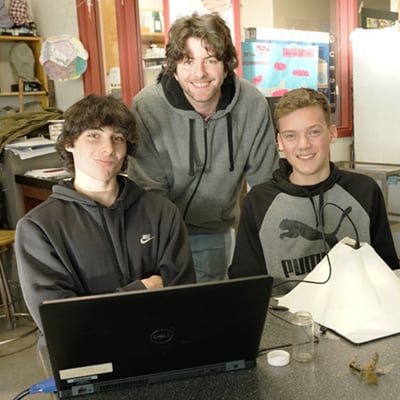 3 high school students smile behind Saturna and a laptop