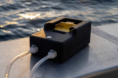 Up close image of a hand-held eDNA sampler resting on the side of a boat at sunset